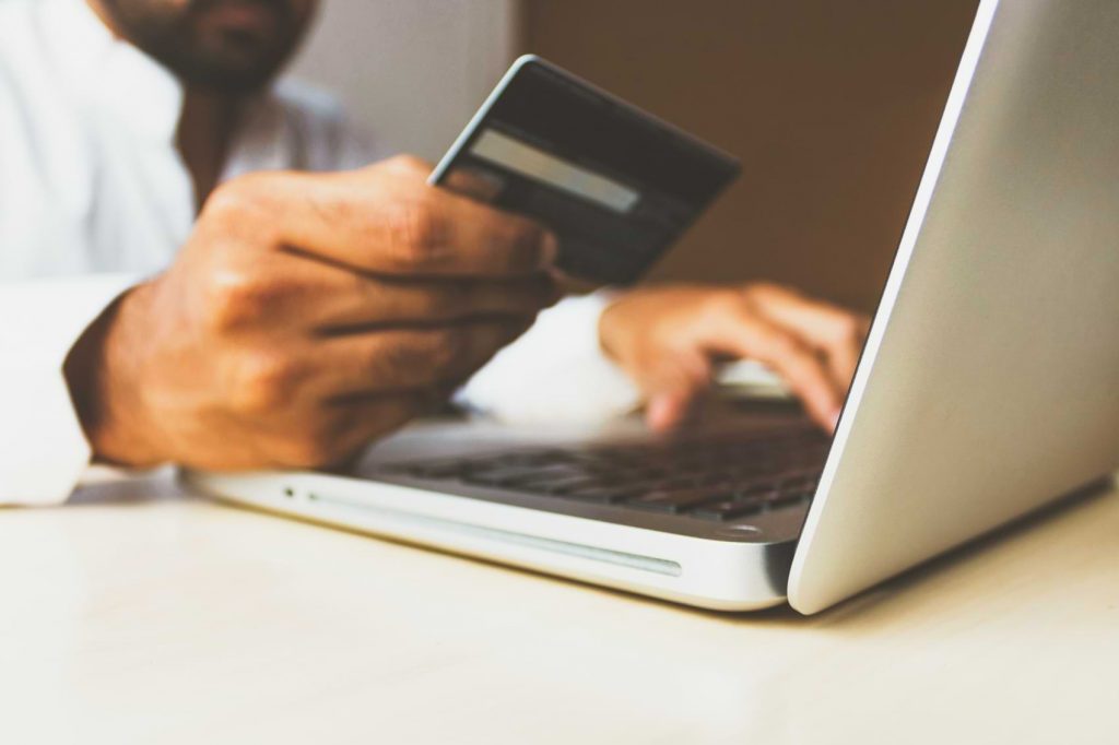 A man carefully copies his credit card information into his laptop, likely making an online purchase