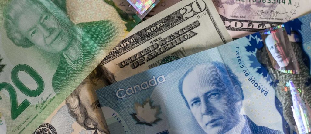 A twenty dollar and five dollar Canadian banknote cover up an American ten dollar bill.