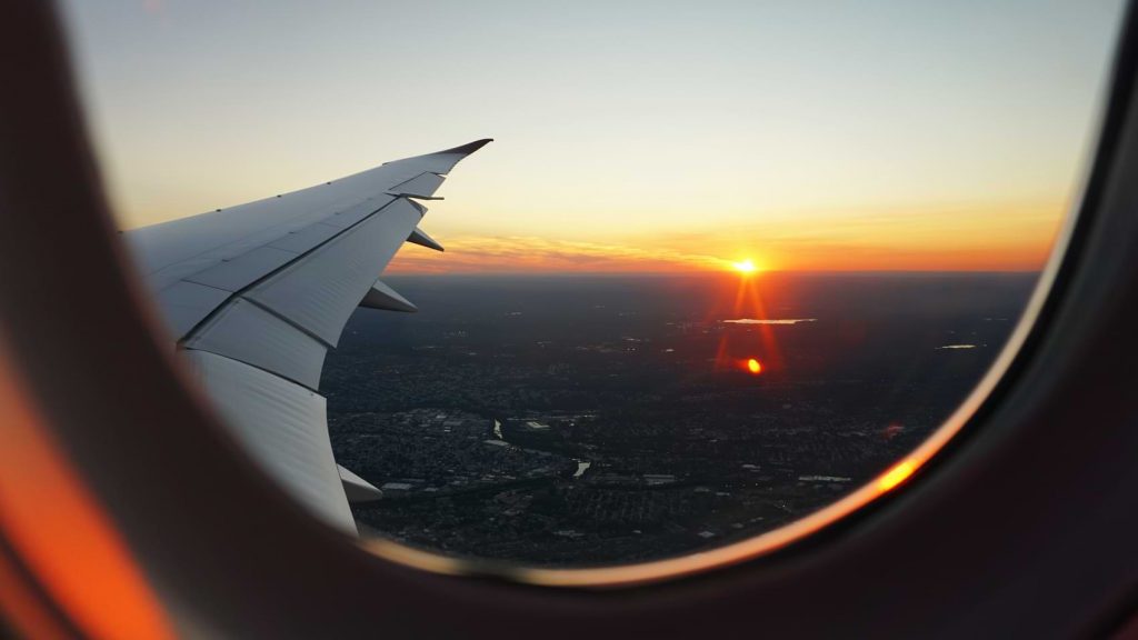 A sunset can be seen lighting up the skyline from the view of an airplane passenger seat.